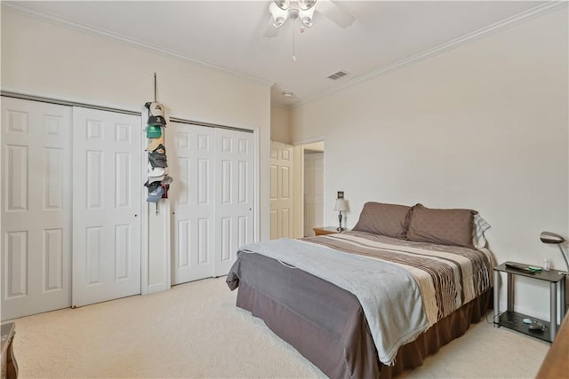 carpeted bedroom featuring ceiling fan, ornamental molding, and two closets