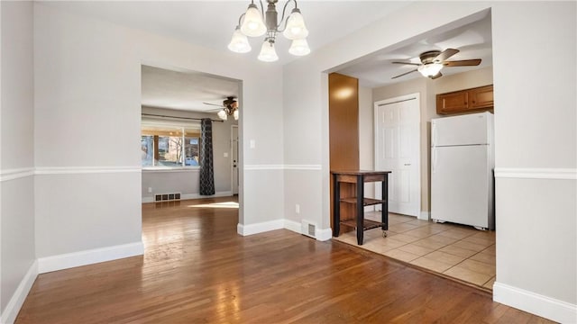 unfurnished dining area with ceiling fan with notable chandelier and light hardwood / wood-style flooring