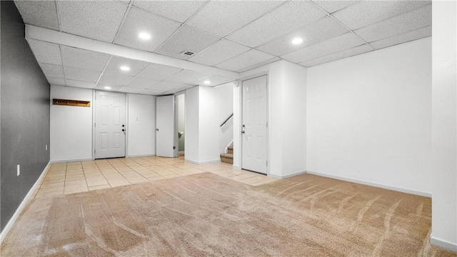 basement with a paneled ceiling and light colored carpet