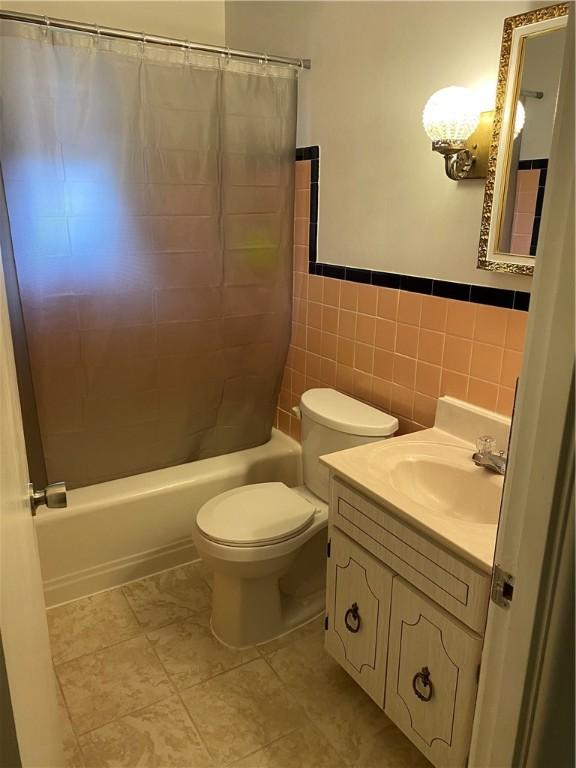 full bathroom featuring tile patterned flooring, toilet, shower / bath combo with shower curtain, vanity, and tile walls