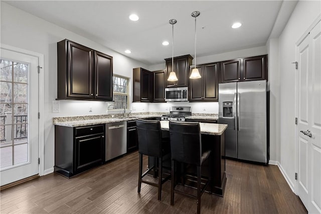 kitchen featuring a kitchen bar, appliances with stainless steel finishes, dark wood-type flooring, a kitchen island, and hanging light fixtures