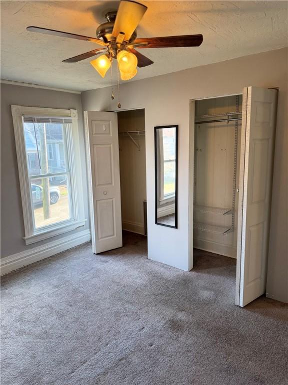 unfurnished bedroom featuring ceiling fan, two closets, dark carpet, and multiple windows