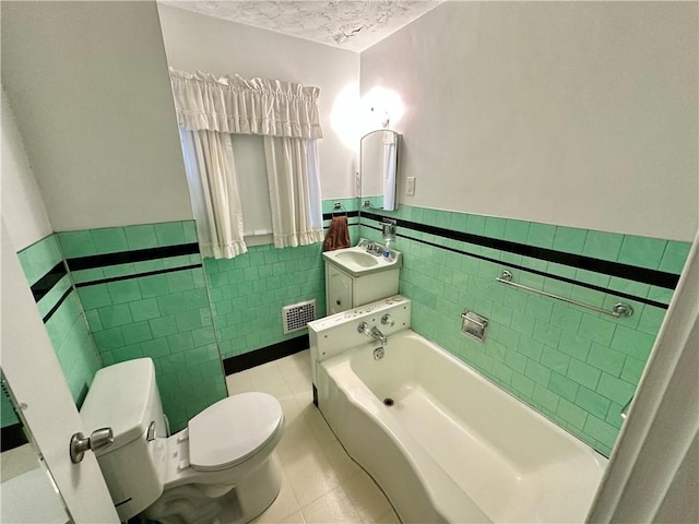 bathroom featuring a tub to relax in, tile patterned floors, toilet, vanity, and tile walls