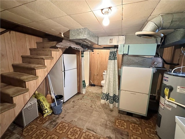 basement featuring heating unit, electric water heater, wooden walls, and white refrigerator