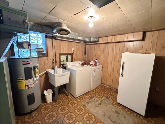 clothes washing area with washer and dryer, sink, wooden walls, and water heater