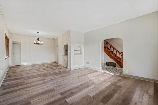 unfurnished living room with built in shelves, wood-type flooring, and an inviting chandelier