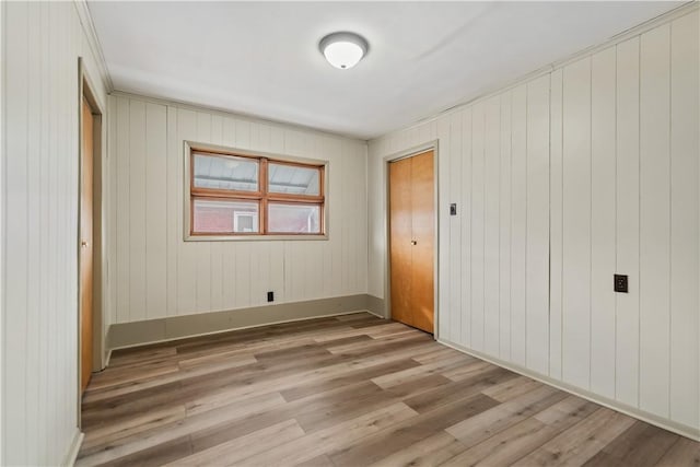 unfurnished bedroom featuring light hardwood / wood-style flooring, a closet, and wood walls