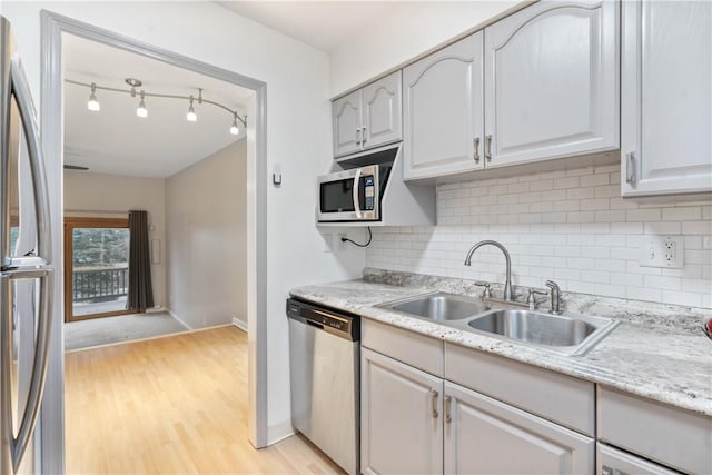 kitchen featuring light wood finished floors, light countertops, decorative backsplash, appliances with stainless steel finishes, and a sink