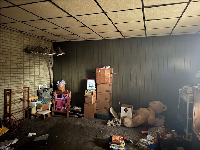 misc room featuring carpet flooring, a paneled ceiling, and wood walls