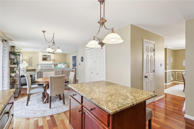 kitchen with hardwood / wood-style floors, decorative light fixtures, a kitchen island, and light stone counters