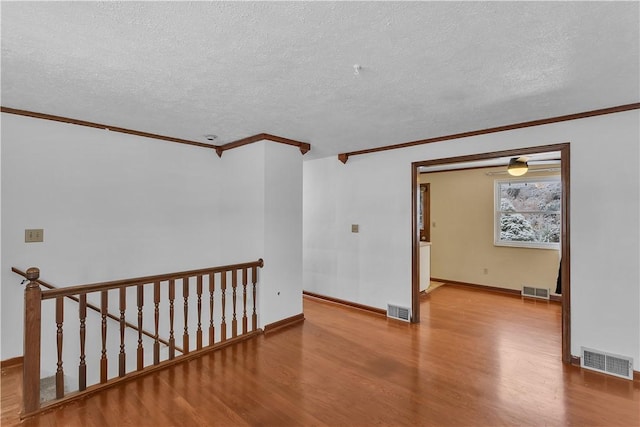 empty room with crown molding, light hardwood / wood-style flooring, and a textured ceiling