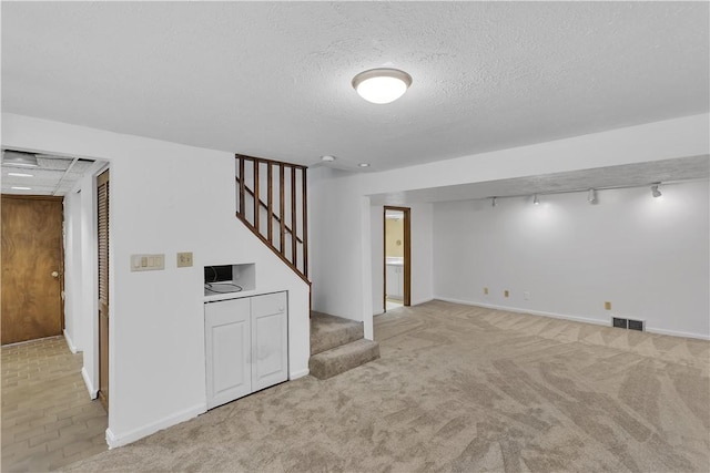 interior space featuring a textured ceiling, light colored carpet, and rail lighting