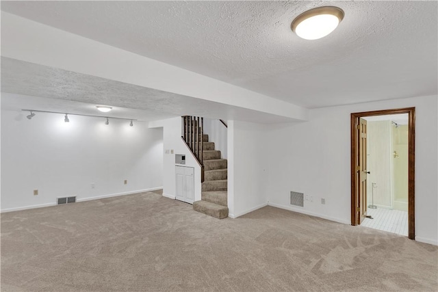 basement featuring a textured ceiling, light carpet, and track lighting