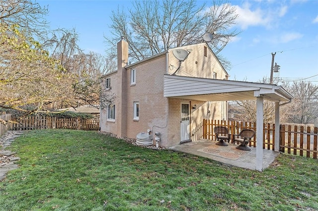 rear view of house with a patio area, a yard, a chimney, a fenced backyard, and brick siding