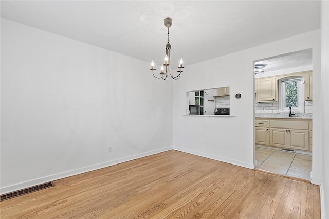 unfurnished dining area featuring sink, a chandelier, and light hardwood / wood-style flooring