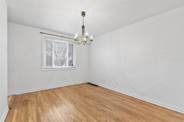 empty room featuring wood finished floors, visible vents, a notable chandelier, and baseboards