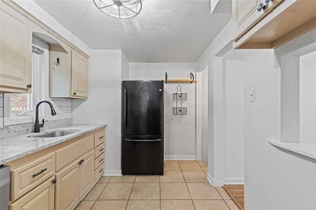 kitchen featuring light tile patterned floors, cream cabinets, freestanding refrigerator, light stone countertops, and a sink