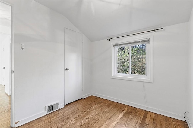 empty room featuring light wood-style flooring, baseboards, lofted ceiling, and visible vents