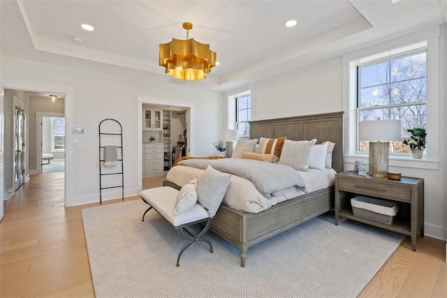 bedroom with light hardwood / wood-style flooring, a raised ceiling, and multiple windows