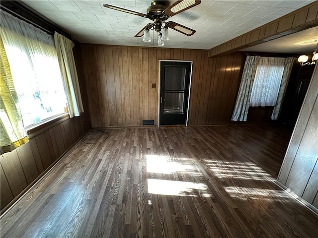 spare room featuring ceiling fan with notable chandelier, dark wood-type flooring, and wood walls