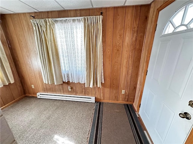 workout room featuring a paneled ceiling, wooden walls, and a baseboard heating unit