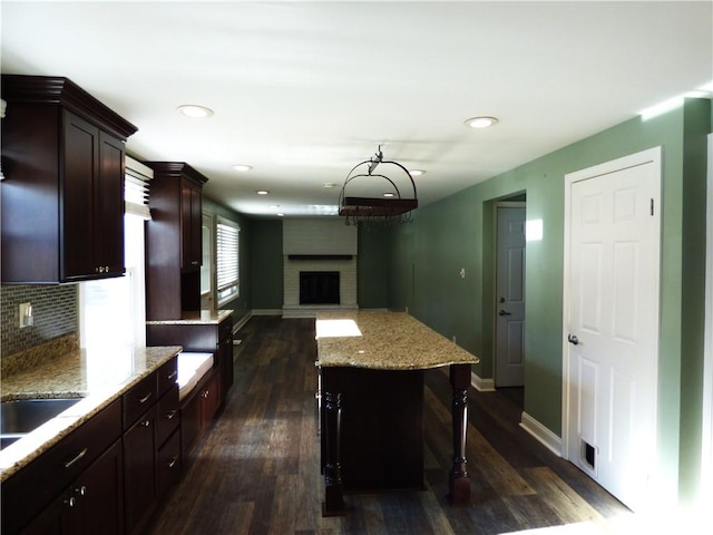 kitchen featuring backsplash, dark wood-type flooring, a kitchen breakfast bar, a brick fireplace, and a kitchen island