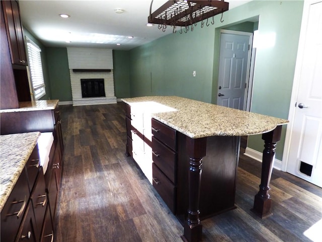 kitchen featuring a kitchen breakfast bar, a brick fireplace, light stone counters, a kitchen island, and dark hardwood / wood-style flooring