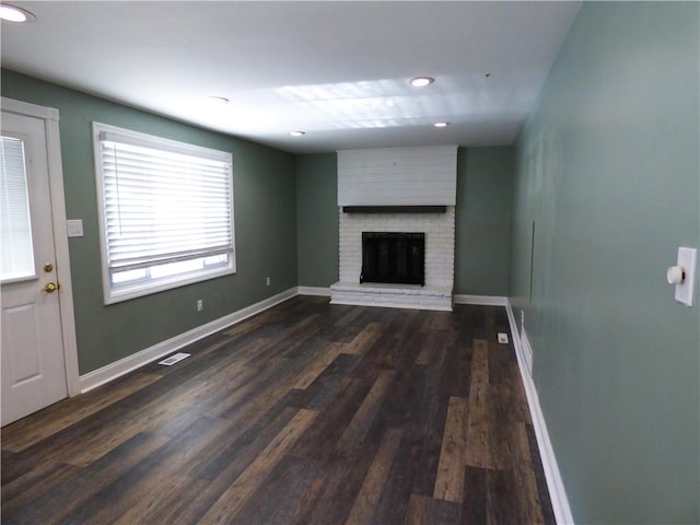 unfurnished living room with dark wood-type flooring and a brick fireplace