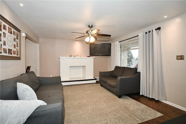 living room featuring ceiling fan, baseboard heating, dark wood-type flooring, and a brick fireplace