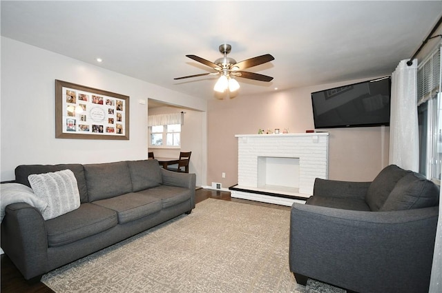 living room with baseboard heating, ceiling fan, a fireplace, and wood-type flooring