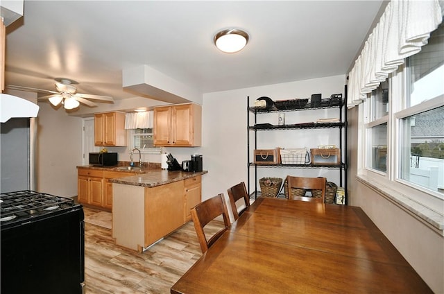 kitchen with ceiling fan, sink, black gas range oven, dark stone countertops, and light hardwood / wood-style floors