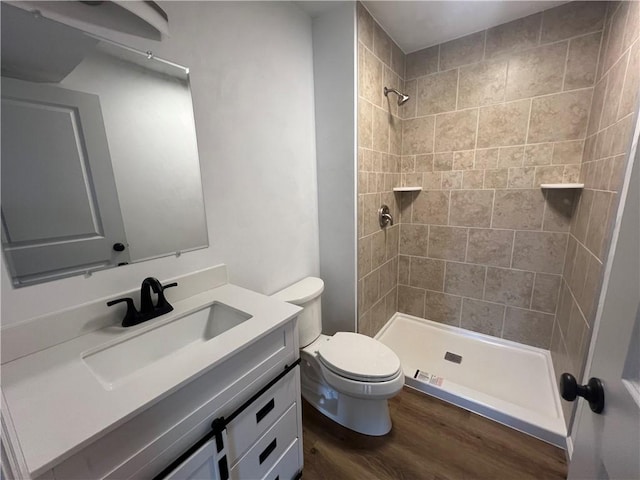 bathroom featuring a tile shower, vanity, wood-type flooring, and toilet