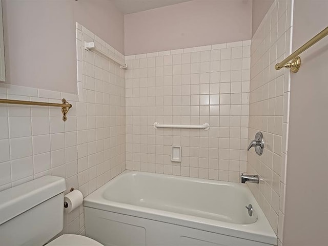 bathroom with tiled shower / bath combo, toilet, and tile walls