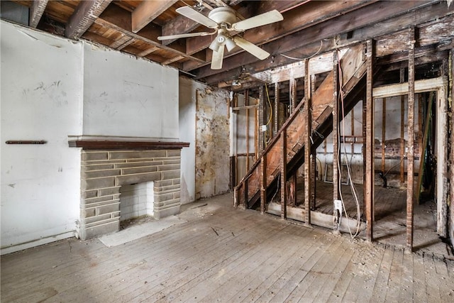 basement featuring ceiling fan, a stone fireplace, and wood-type flooring