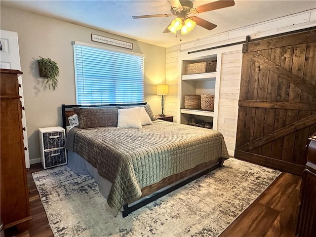 bedroom with ceiling fan, a barn door, and dark hardwood / wood-style floors