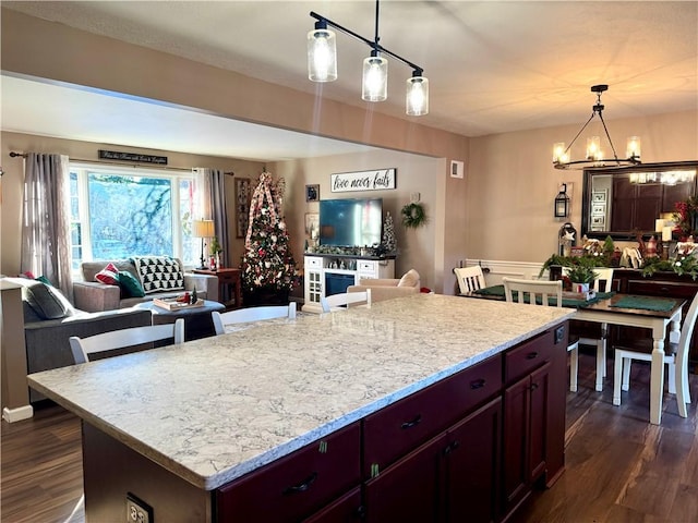 kitchen with a center island, light stone counters, dark hardwood / wood-style floors, a notable chandelier, and decorative light fixtures