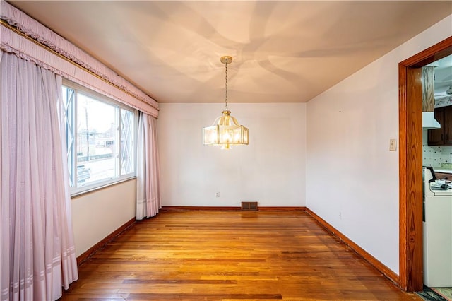 unfurnished dining area with hardwood / wood-style flooring, washer / clothes dryer, and a notable chandelier