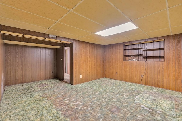 basement featuring carpet flooring, a paneled ceiling, and wooden walls