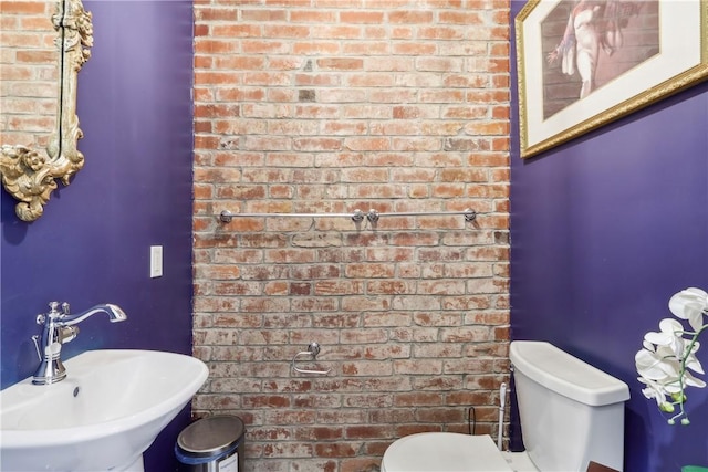 bathroom with sink, brick wall, and toilet