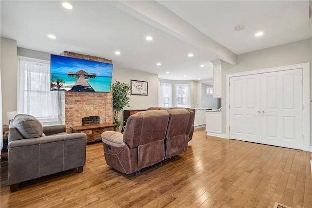 living room featuring beam ceiling, light hardwood / wood-style floors, and a fireplace