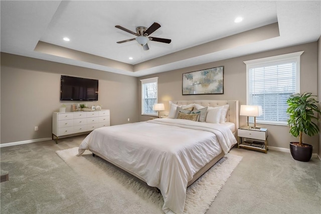 bedroom with ceiling fan, a raised ceiling, and light carpet