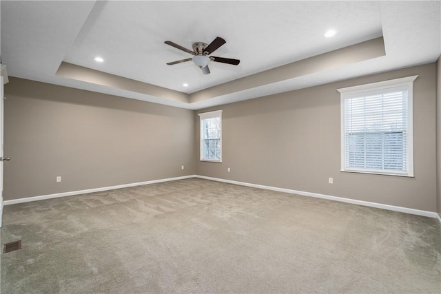 carpeted empty room featuring a raised ceiling, ceiling fan, and plenty of natural light