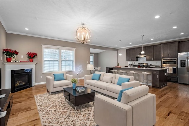 living room featuring sink, a high end fireplace, a notable chandelier, crown molding, and light hardwood / wood-style floors