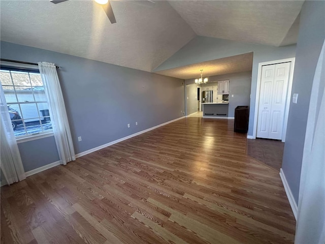 unfurnished living room with a textured ceiling, ceiling fan with notable chandelier, dark wood-type flooring, and vaulted ceiling