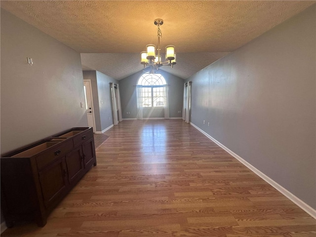 unfurnished dining area with a textured ceiling, lofted ceiling, a notable chandelier, and hardwood / wood-style flooring