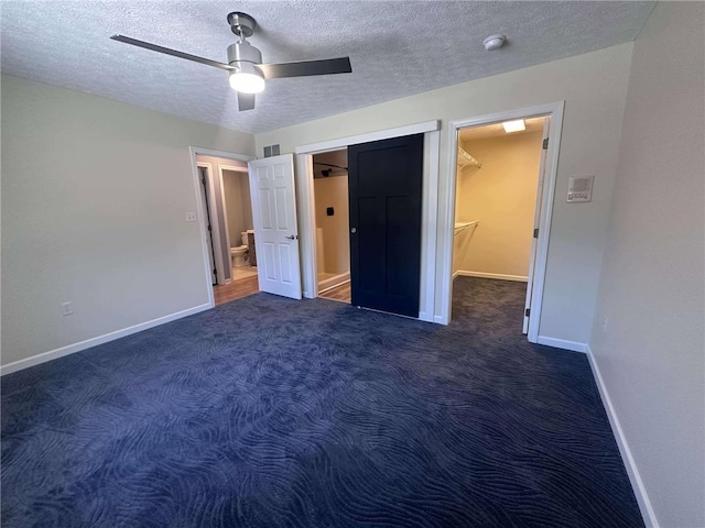 unfurnished bedroom with ceiling fan, dark carpet, a spacious closet, and a textured ceiling