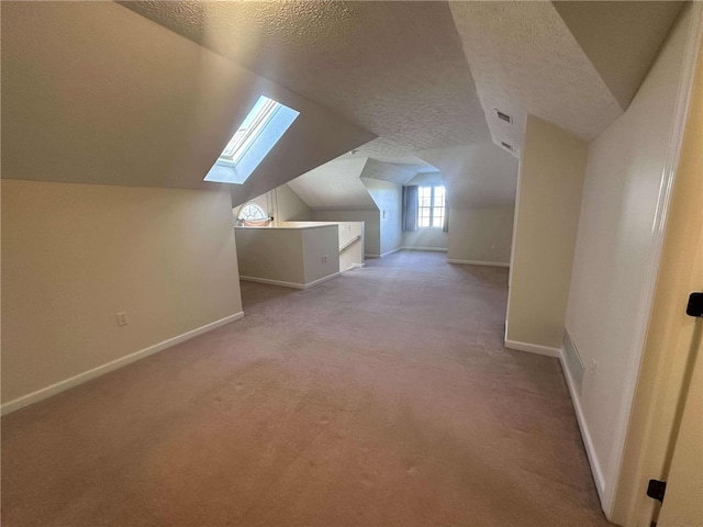 additional living space featuring light carpet, a textured ceiling, and vaulted ceiling with skylight