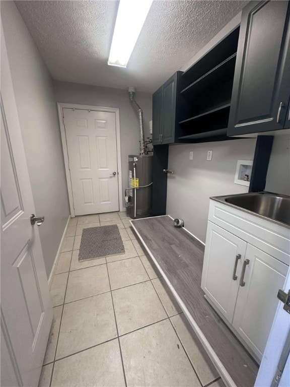 laundry area with gas water heater, light tile patterned floors, a textured ceiling, and hookup for a washing machine