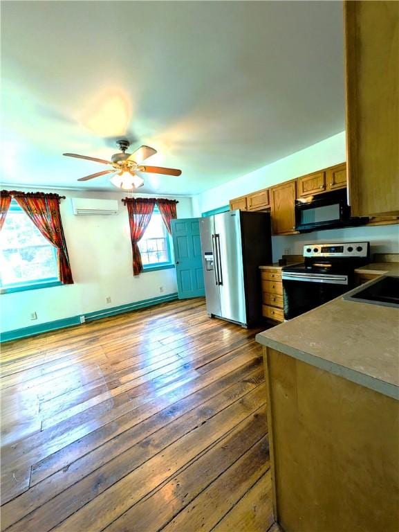 kitchen with a wall mounted air conditioner, appliances with stainless steel finishes, dark hardwood / wood-style flooring, ceiling fan, and sink