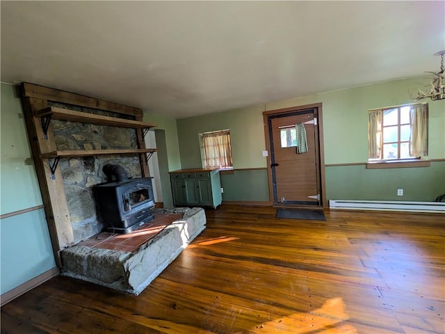 unfurnished living room with dark hardwood / wood-style flooring, a wood stove, baseboard heating, and an inviting chandelier